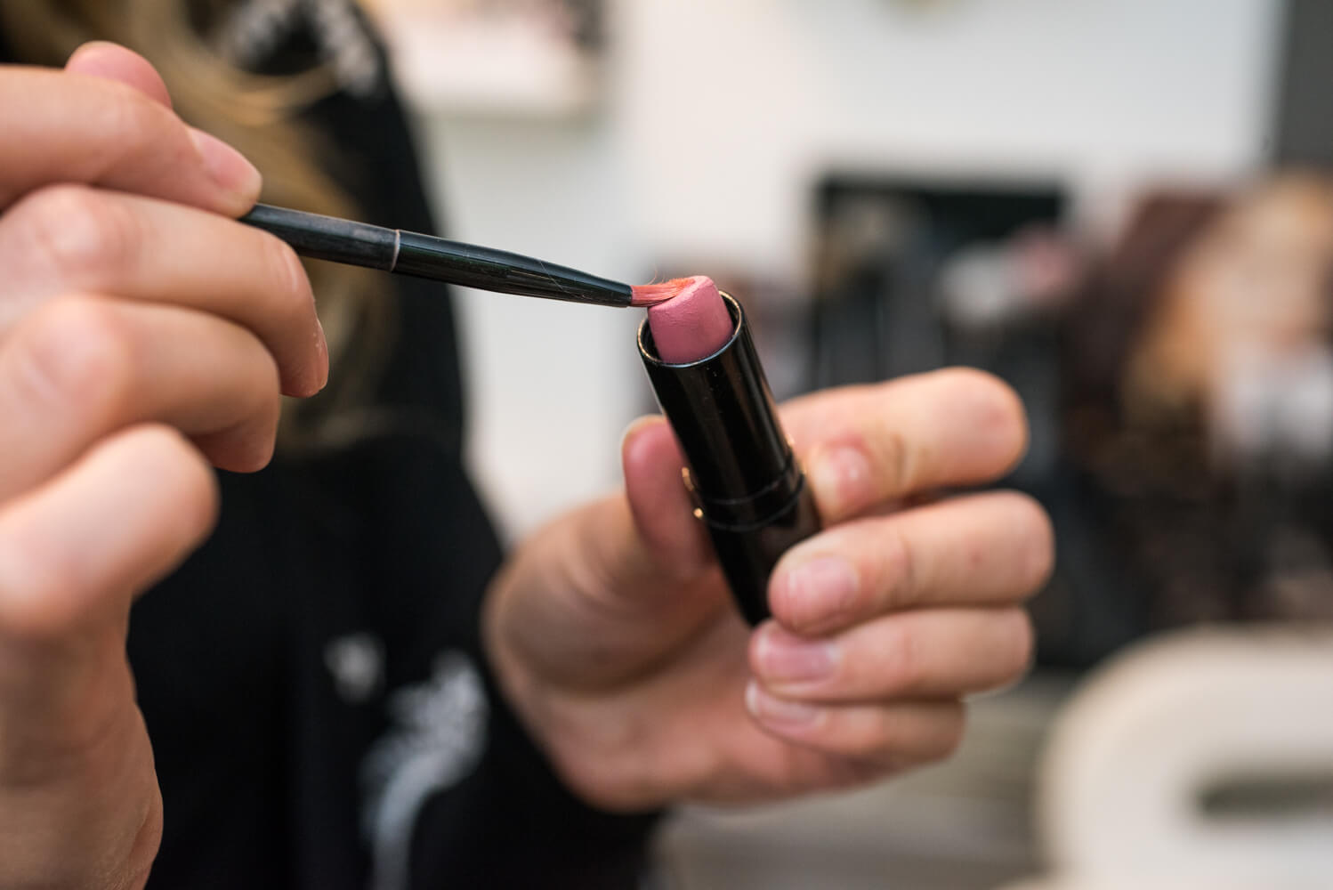 Young woman applying lipstick with brush